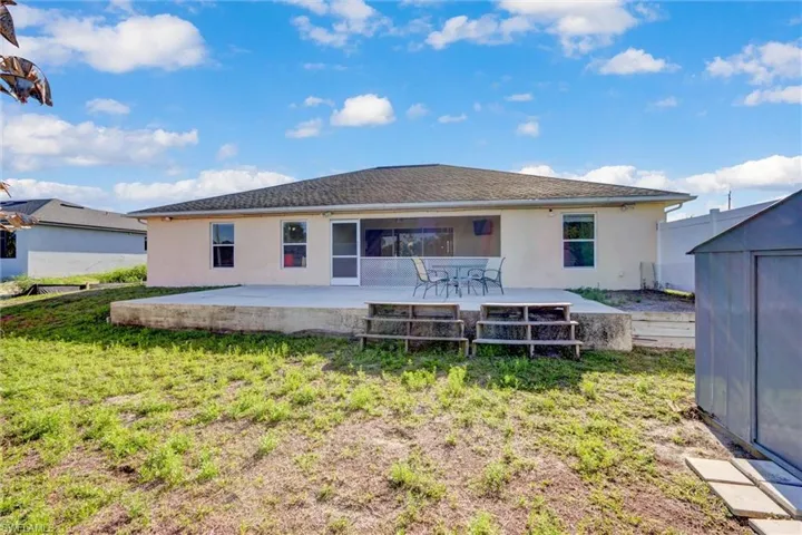 Back of house featuring a patio, stucco siding, a storage unit, and a lawn
