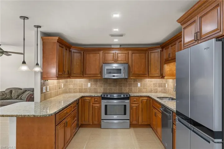 Kitchen with granite countertops, backsplash, stainless steel appliances, sink, and pendant lighting