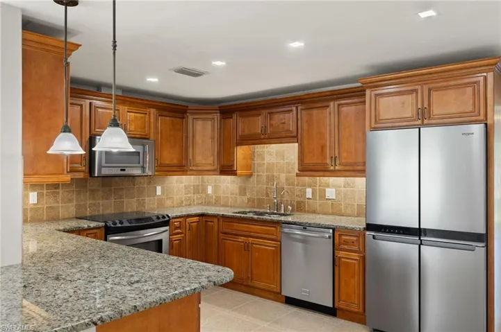 Kitchen with granite countertops, backsplash, stainless steel appliances, sink, and pendant lighting