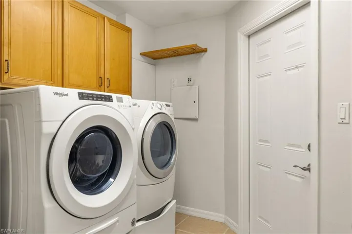 Laundry room featuring separate washer and dryer, light tile patterned floors, and cabinets