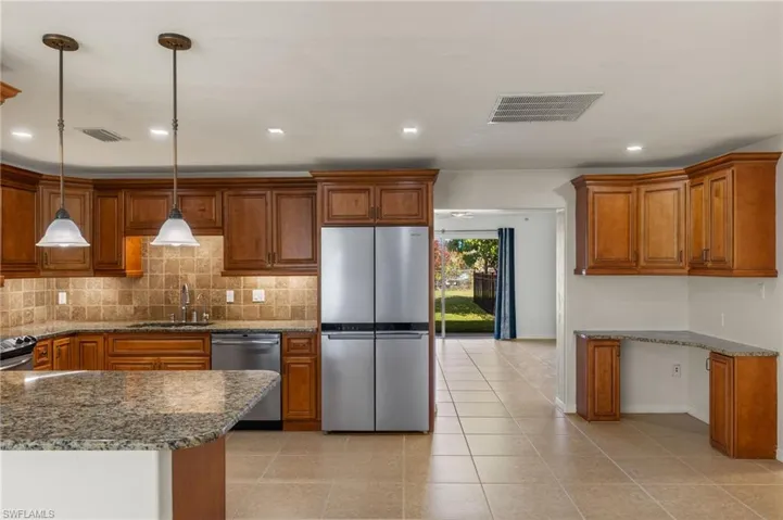 Kitchen with granite countertops, backsplash, stainless steel appliances, sink, and pendant lighting