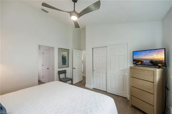 Vaulted ceiling with a ceiling fan, white paneled doors, and wood-finish flooring