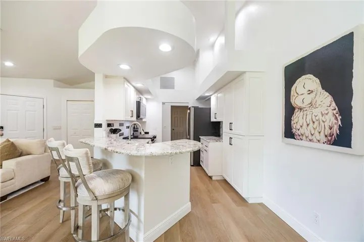 Kitchen featuring a curved breakfast bar with a speckled countertop, white cabinetry, a stainless steel sink with a gooseneck faucet, and light wood-finish flooring