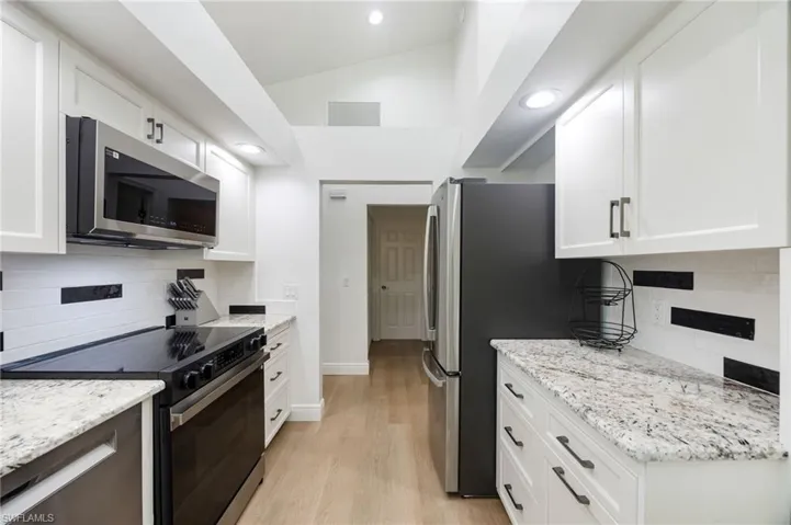 Kitchen featuring stainless steel appliances, white cabinetry with dark hardware, light-toned wood-finish flooring, granite countertops, and vaulted ceilings