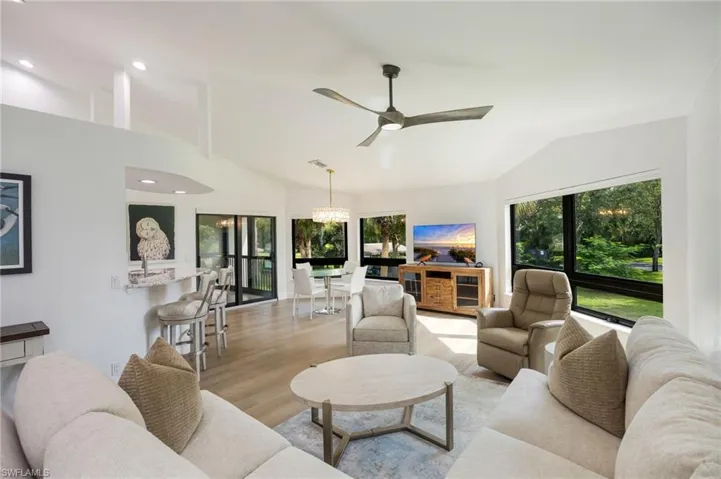 Vaulted ceiling with a contemporary ceiling fan, wood-finish flooring, a breakfast bar with stone-finish countertop, and large windows