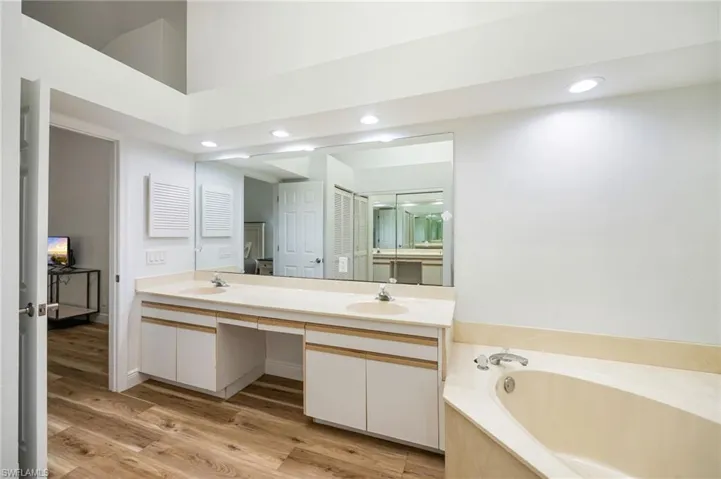 Dual vanity with integrated sinks, wood-finish flooring, recessed lighting, and built-in bathtub