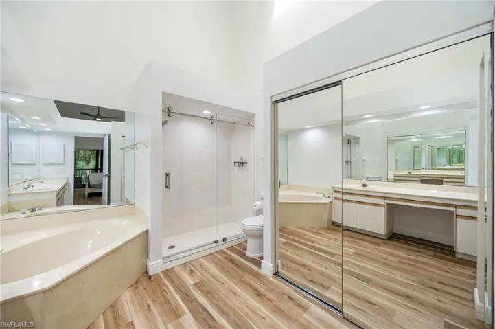 Vaulted ceiling, wood-finish flooring, corner soaking tub, glass-enclosed shower with subway tile, and mirrored sliding closet doors