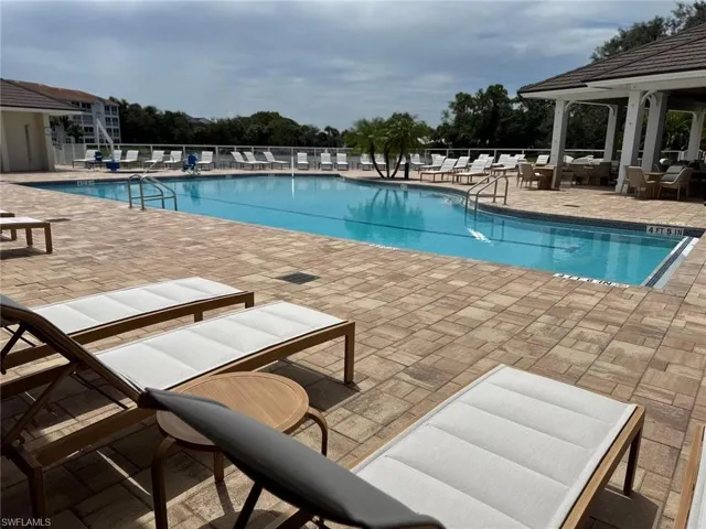 Community swimming pool with a surrounding paver deck, a covered lounge area with a tile roof, and integrated pool steps