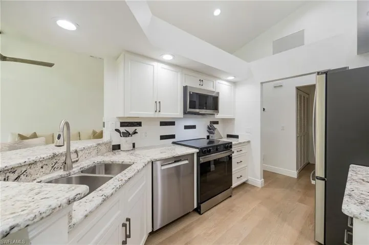 White cabinetry with sleek hardware, granite countertops, stainless steel appliances, wood-finish flooring, and recessed lighting