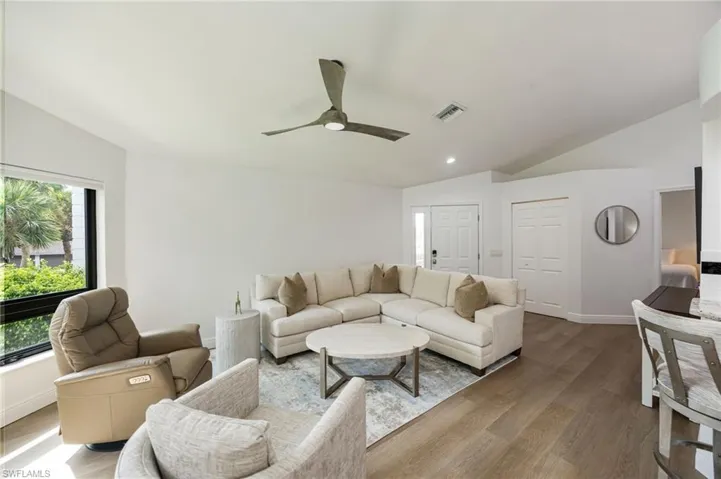 Vaulted ceiling with a contemporary ceiling fan, large window, wood-finish flooring, and white walls