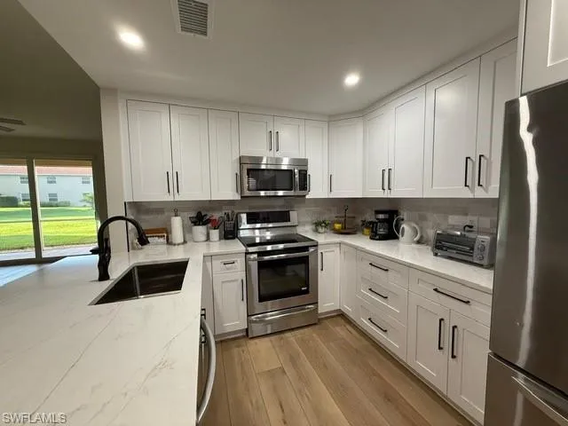 Kitchen with appliances with stainless steel finishes, white cabinetry, light stone counters, light wood finished floors, and recessed lighting
