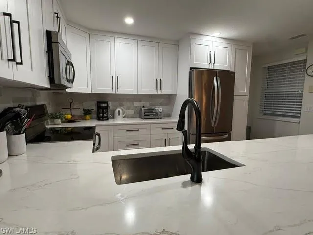Kitchen with white cabinetry, light stone counters, appliances with stainless steel finishes, and tasteful backsplash