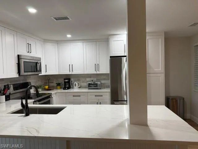 Kitchen featuring light stone countertops, white cabinetry, stainless steel appliances, a peninsula, and recessed lighting