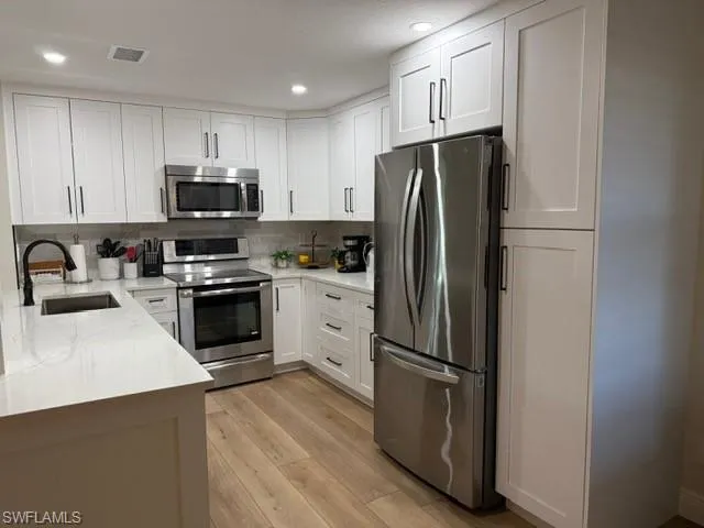 Kitchen with appliances with stainless steel finishes, white cabinetry, light stone countertops, recessed lighting, and light wood-style floors