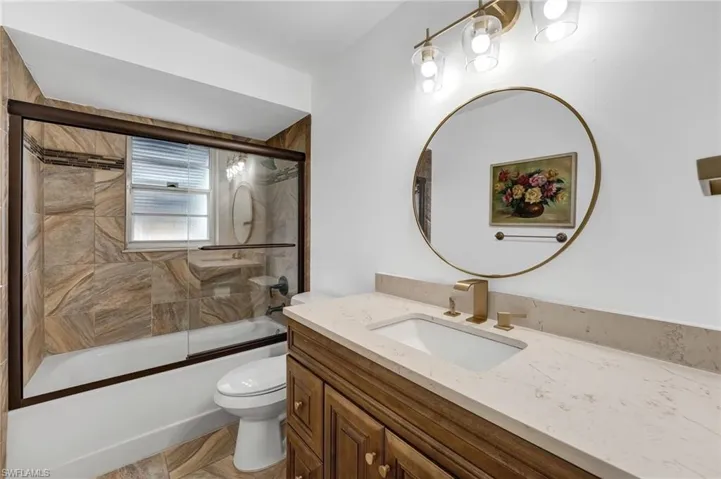 The second full bathroom features a shower/tub combination with a glass enclosure, quartz countertops, and gold-accent fixtures, complemented by spectacular porcelain tile walls. This well-appointed bath is shared by the second and third bedrooms.