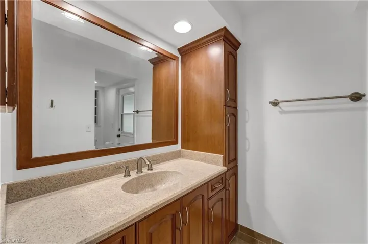 Serving as a pool bath, the primary bathroom includes a single vanity and a stunning walk-in shower with a seamless glass enclosure and elegant floor-to-ceiling porcelain tile.