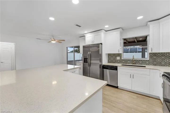 This beautifully remodeled kitchen showcases sparkling white quartz countertops, stainless steel appliances, custom cabinetry with soft-close doors and drawers, a spectacular backsplash, and recessed lighting. A convenient pass-through window makes entertaining effortless.