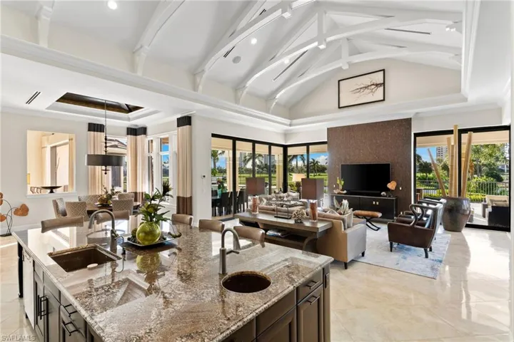 Kitchen with light stone counters, open floor plan, decorative light fixtures, a high ceiling, and an island with sink