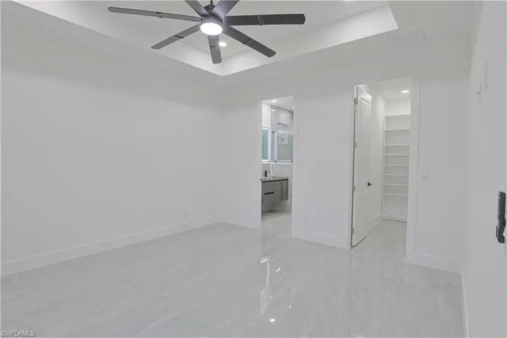 Unfurnished bedroom with a spacious closet, a raised ceiling, ceiling fan, and recessed lighting
