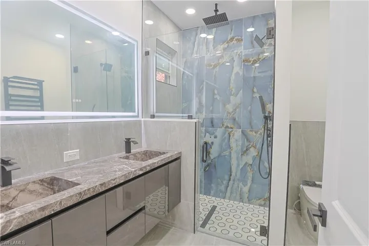 Full bathroom featuring a marble finish shower, double vanity, tile walls, and recessed lighting