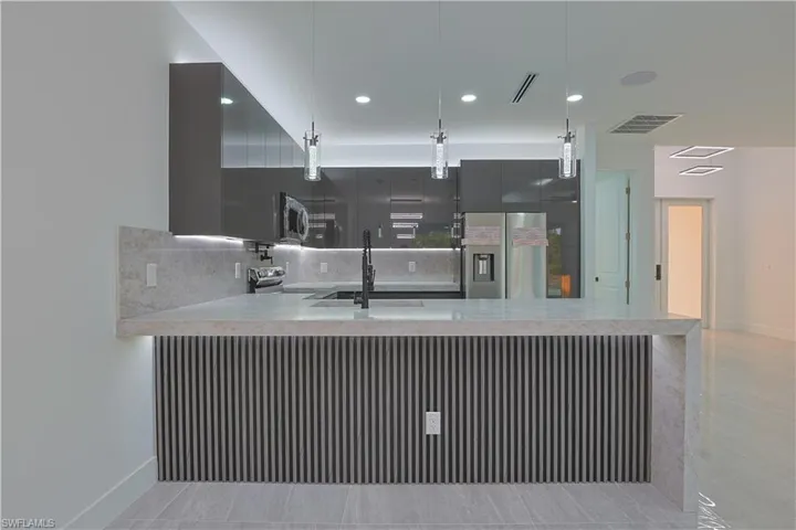 Kitchen featuring modern cabinets, light stone counters, backsplash, pendant lighting, and stainless steel appliances