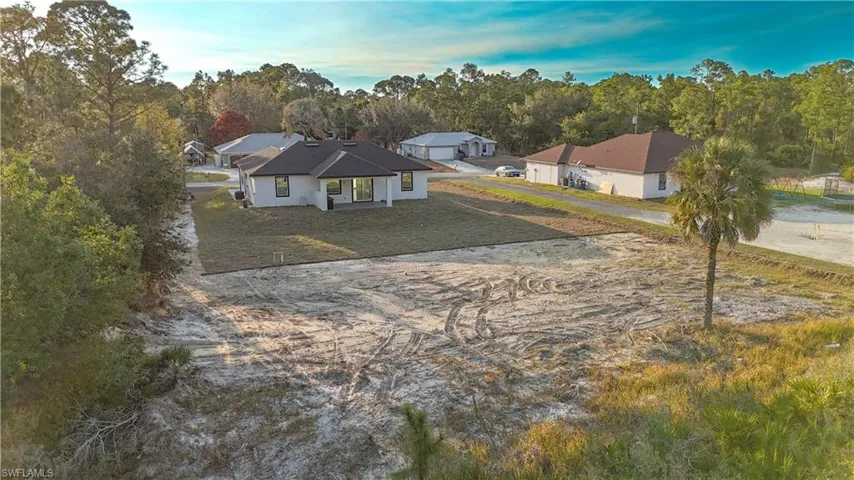View of front of house with a patio area, a front lawn, dirt driveway, and view of scattered trees