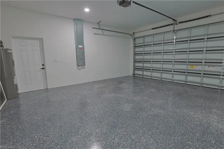 Garage with water heater, electric panel, and a garage door opener