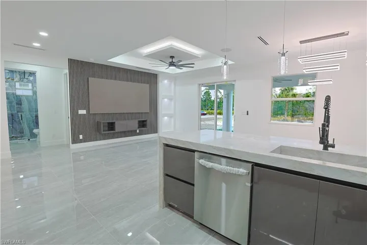 Kitchen featuring light stone countertops, dishwasher, a tray ceiling, pendant lighting, and open floor plan