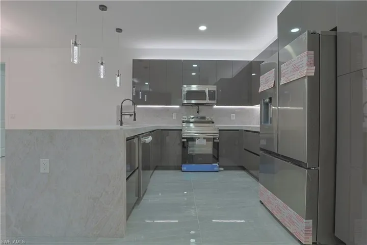 Kitchen featuring stainless steel appliances, light stone countertops, modern cabinets, and pendant lighting