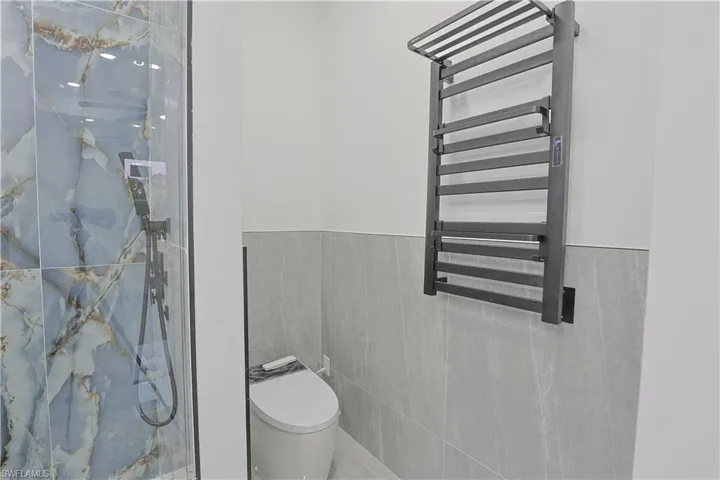 Bathroom with a towel warming rack, radiator, a marble finish shower, tile walls, and wainscoting