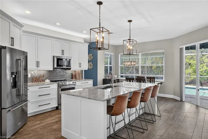 Kitchen with stainless steel appliances, light stone counters, decorative backsplash, and dark wood-style floors