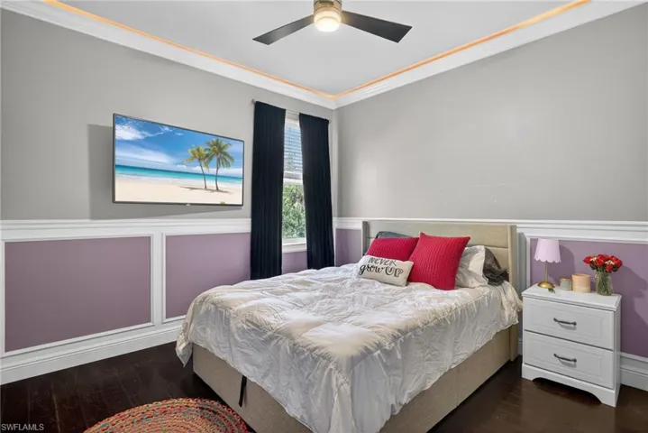 Bedroom with crown molding, dark wood-style flooring, a decorative wall, wainscoting, and ceiling fan