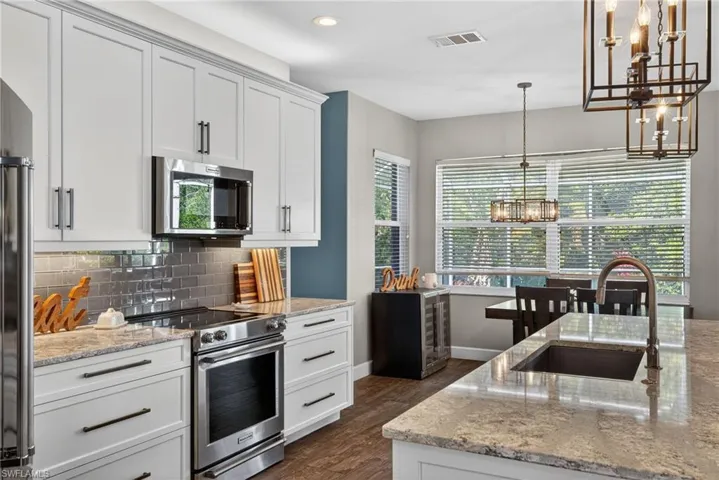 Kitchen featuring stainless steel appliances, light stone countertops, white cabinetry, and dark wood-type flooring
