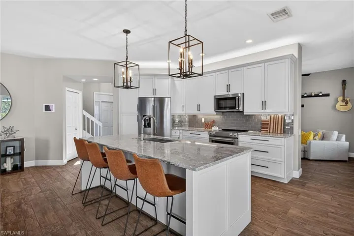 Kitchen featuring dark wood-style floors, light stone countertops, a kitchen bar, and stainless steel appliances