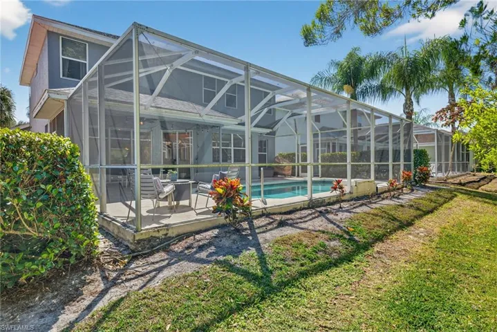 Back of property with a patio area, a sunroom, an outdoor pool, glass enclosure, and a yard