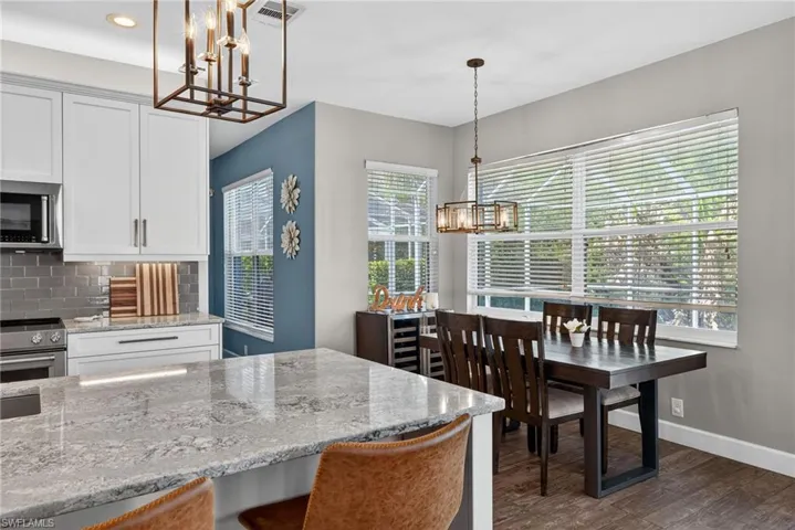 Kitchen featuring hanging lights, white cabinets, stainless steel appliances, light stone countertops, and dark wood-style floors