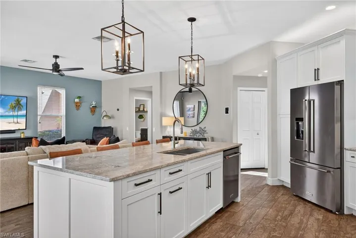 Kitchen featuring open floor plan, a kitchen island with sink, light stone countertops, white cabinets, and stainless steel appliances