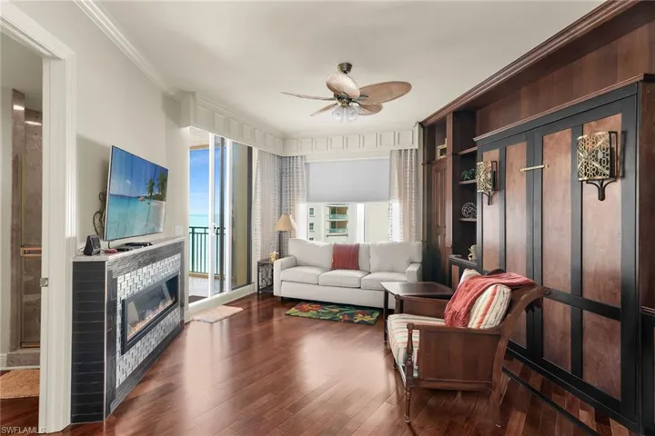 Living room featuring crown molding, a ceiling fan, dark wood-style floors, and a glass covered fireplace