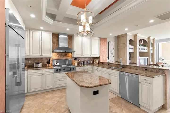 Kitchen with dark stone counters, coffered ceiling, stainless steel appliances, a peninsula, and crown molding