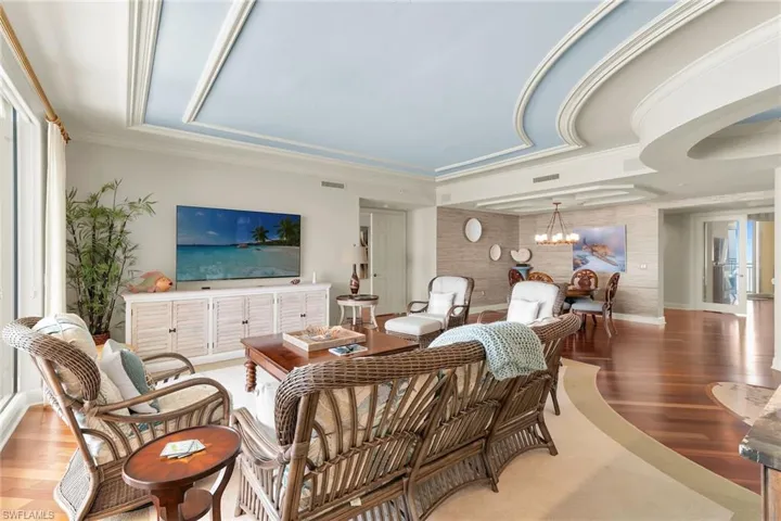 Living area featuring wood finished floors, ornamental molding, hanging lights, and a raised ceiling