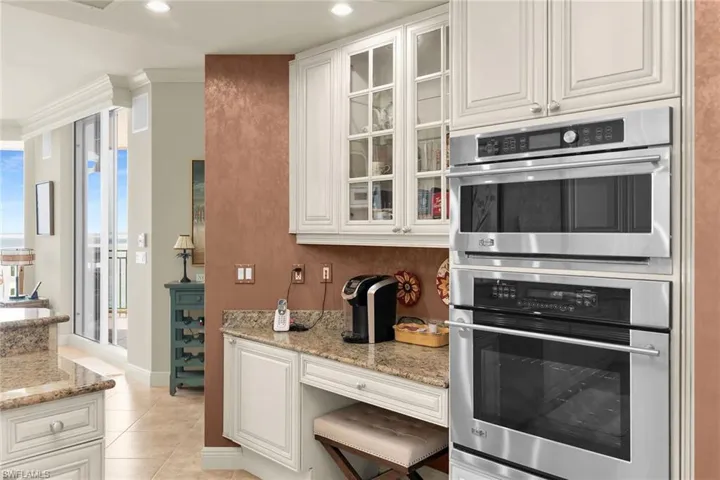 Kitchen featuring double oven, glass fronted cabinets, white cabinets, light stone counters, and ornamental molding