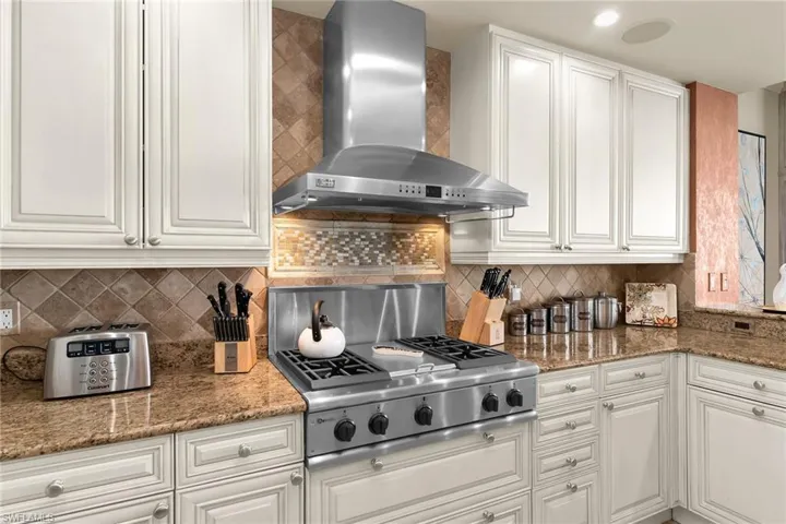 Kitchen with dark stone countertops, stainless steel gas stovetop, white cabinets, and tasteful backsplash