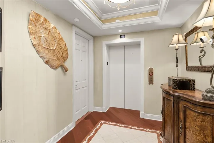 Doorway to outside with a raised ceiling, inlaid floor details, elevator, crown molding, and wood finished floors