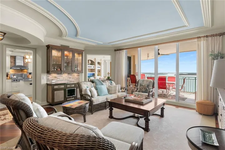 Living room featuring a water view, a raised ceiling, light wood-style flooring, a dry bar, and ornamental molding