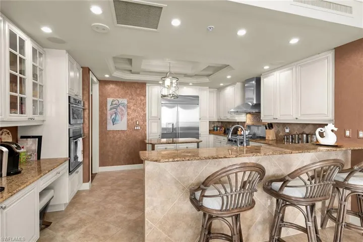 Kitchen featuring light stone counters, a breakfast bar, glass fronted cabinets, a peninsula, and backsplash