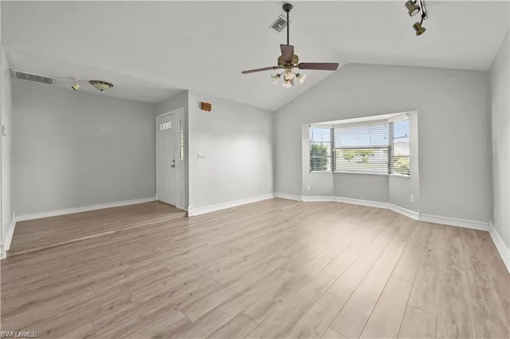 Empty room with lofted ceiling, track lighting, ceiling fan, and light hardwood / wood-style floors