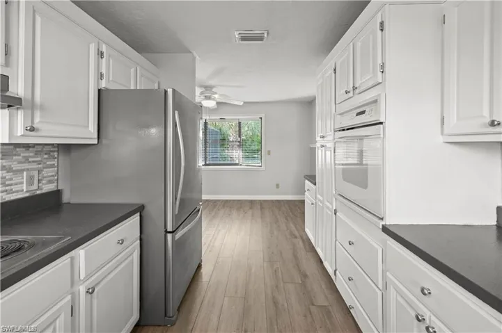 Kitchen with ceiling fan, white oven, light hardwood / wood-style flooring, and white cabinetry