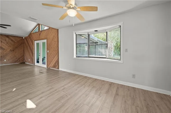 Spare room with wood walls, ceiling fan, vaulted ceiling, and light wood-type flooring