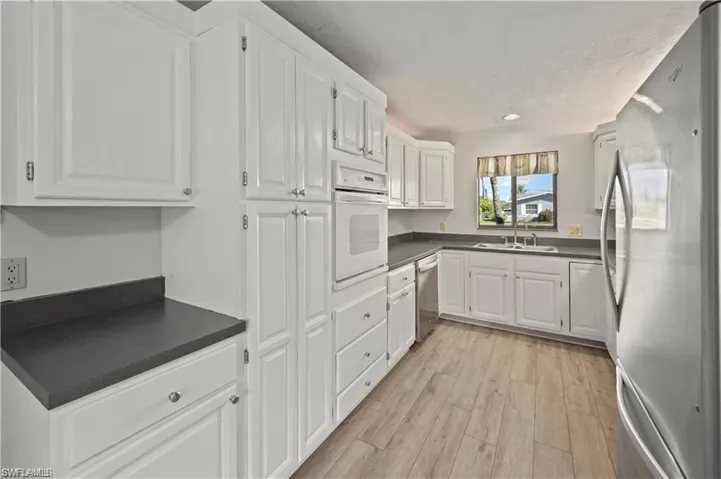 Kitchen with white cabinets, stainless steel appliances, sink, and light hardwood / wood-style floors