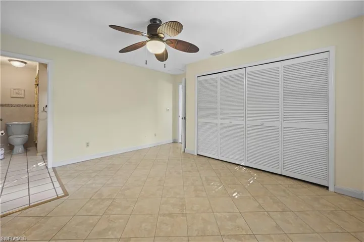 Unfurnished bedroom featuring ceiling fan, light tile patterned flooring, ensuite bath, and a closet